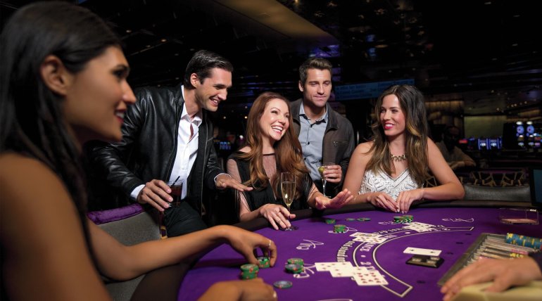 Три красивых женщины в вечерних нарядах играют в покер, а их мужчины оказывают поддержку и подсказывают, как совершать ставки