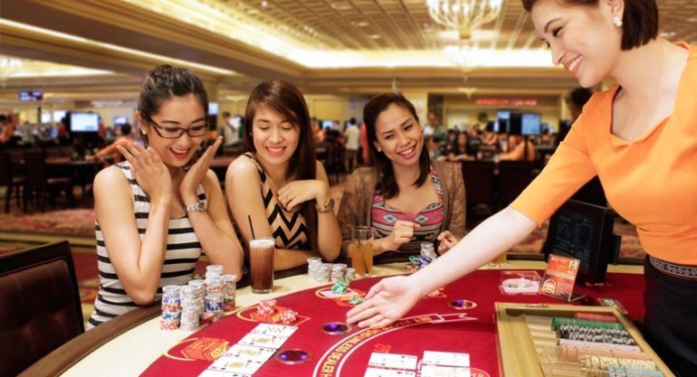 Три симпатичных азиатских девушки веселятся за игрой в блэкджек, распивая коктейли