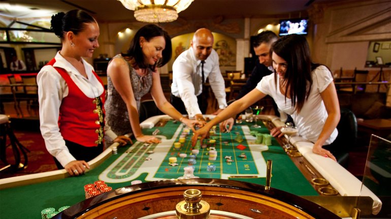 Девушка крупье в строгой форме ведет игру в рулетку для гостей казино