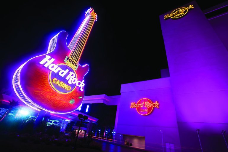 Огромная вывеска казино в виде гитары с неоновой подсветкой и с надписью "Hard Rock"