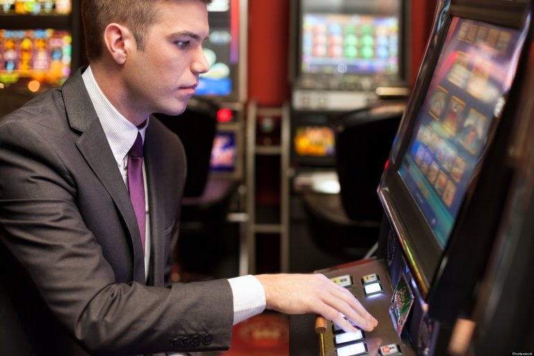 Молодой мужчина в деловой одежде играет на автомате в казино