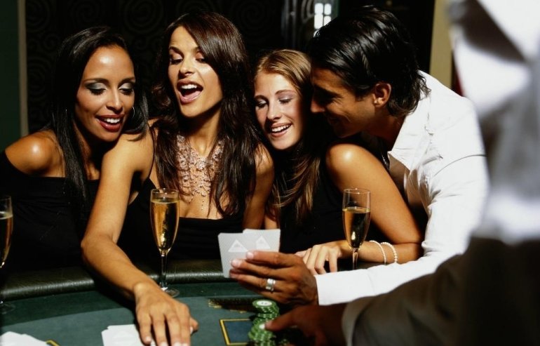 Три красотки навеселе и молодой мужчина играют в покер за бокалом шампанского