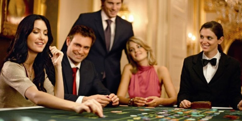 Блондинка и брюнетка в вечерних платьях в компании своих мужчин играют в рулетку в казино вип-уровня